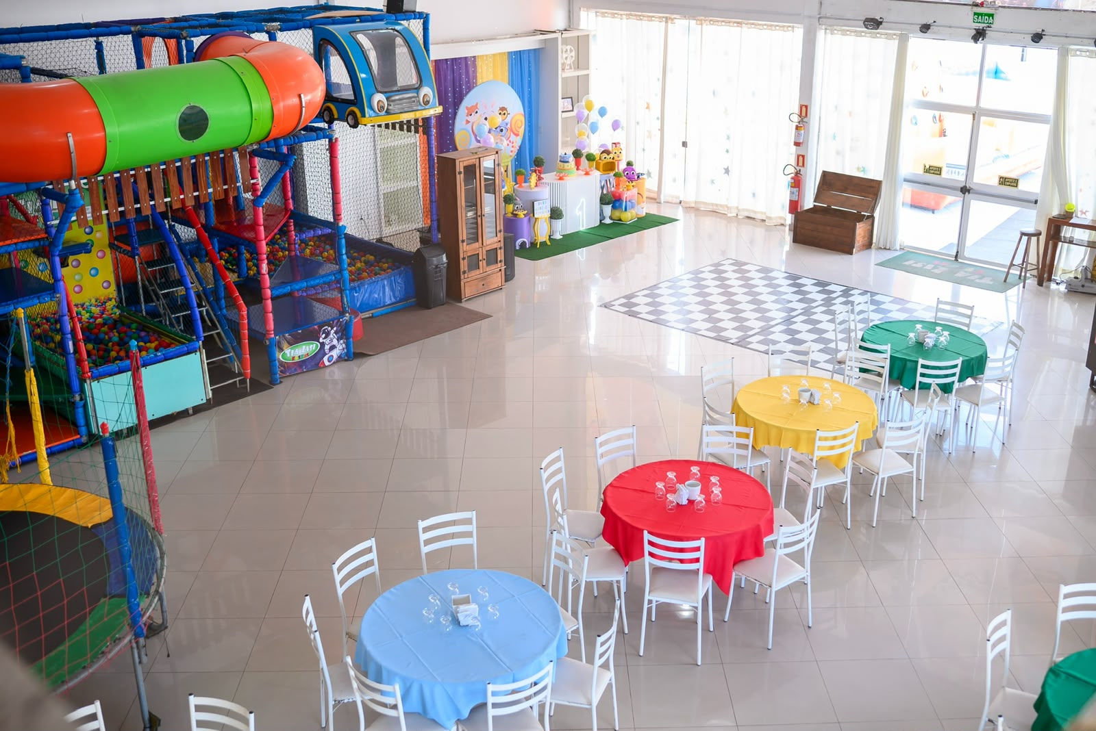 Salão de festas amplo com mesas coloridas e playground